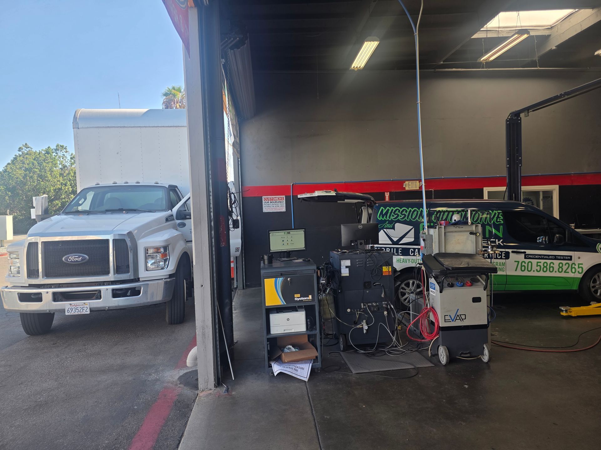 Truck parked beside auto repair shop with equipment and a green-and-white vehicle inside the garage