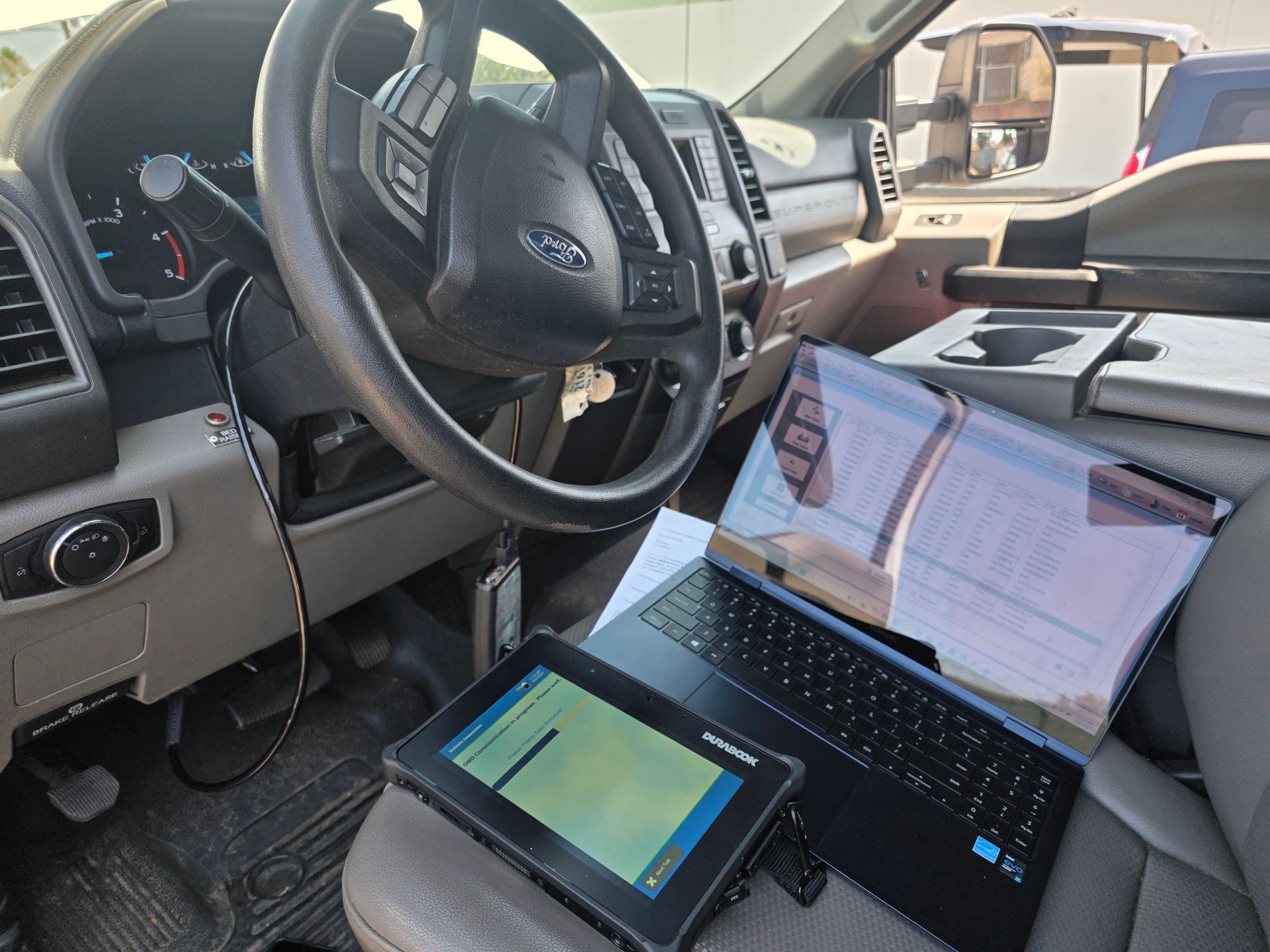 Laptop and tablet open on a vehicle seat, showing maps and a car dashboard in the background