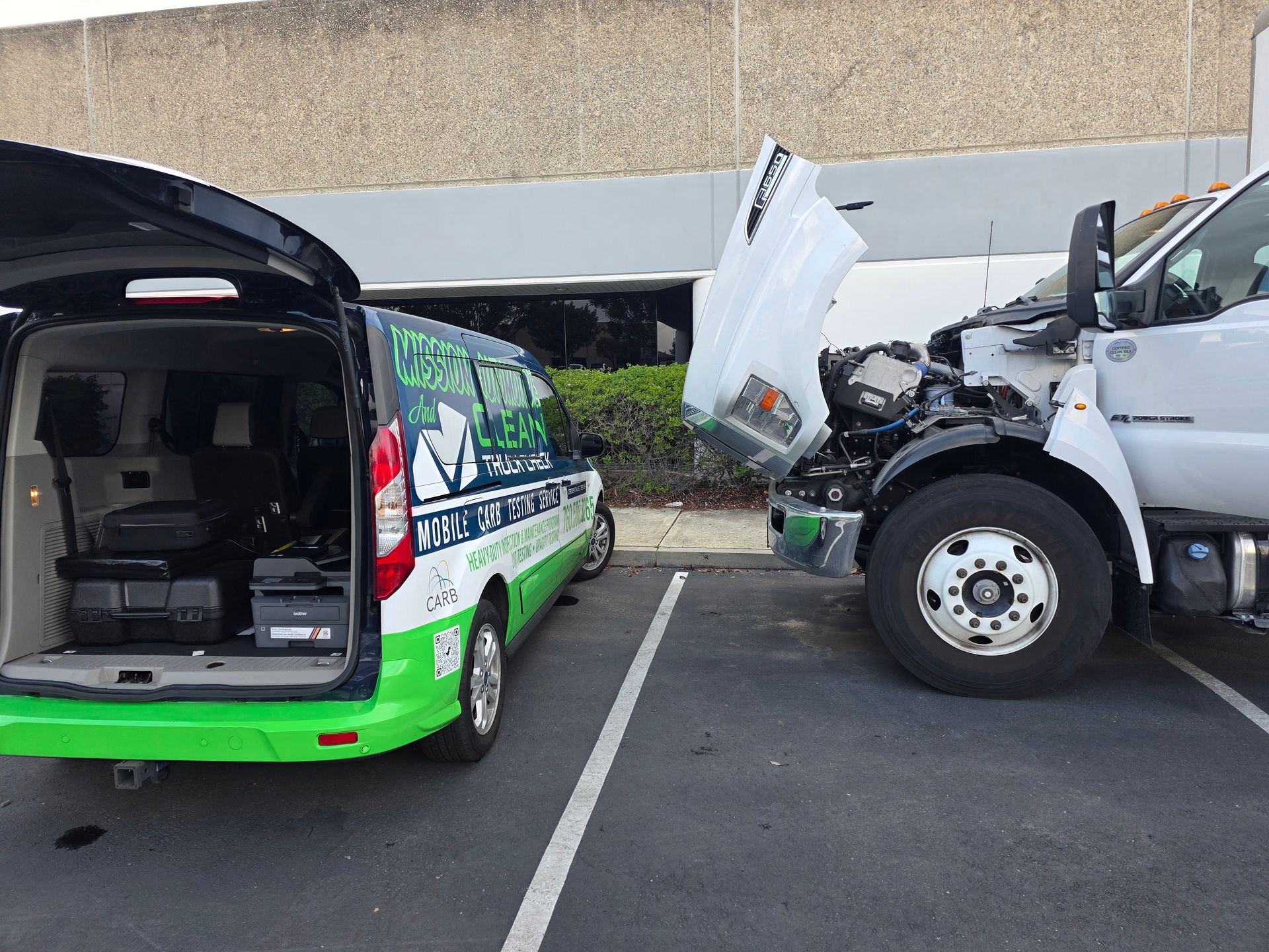 Damaged green van and white truck in parking lot after collision, with the truck’s hood crumpled open