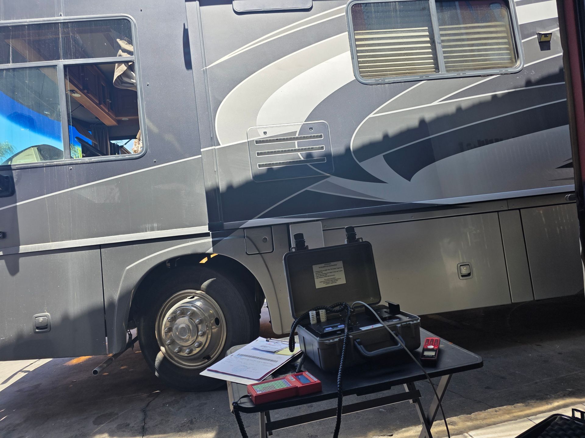 White RV parked beside a table with camping gear, including a laptop and a red item.