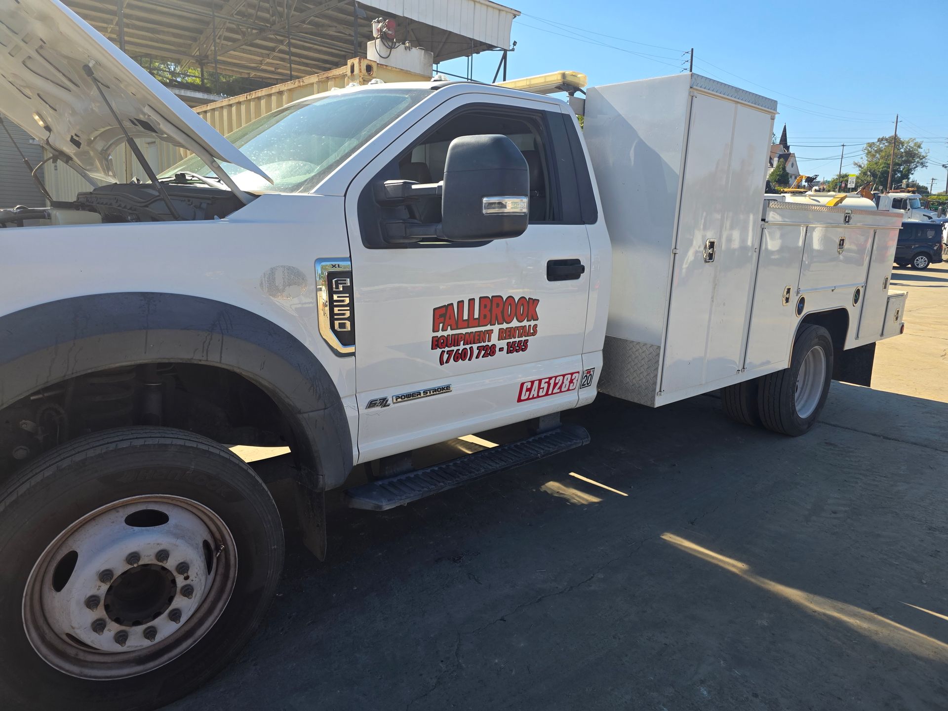 White utility truck parked on a street with storage compartments and company logos on the door.