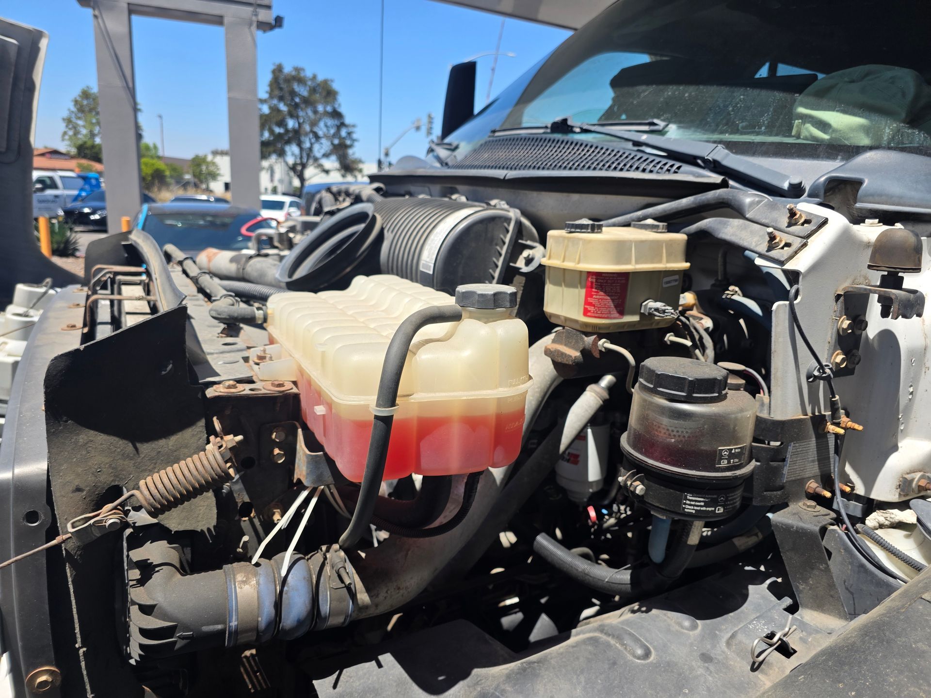 Damaged car engine bay with exposed hoses, fluid reservoirs, and removed front body panels outdoors