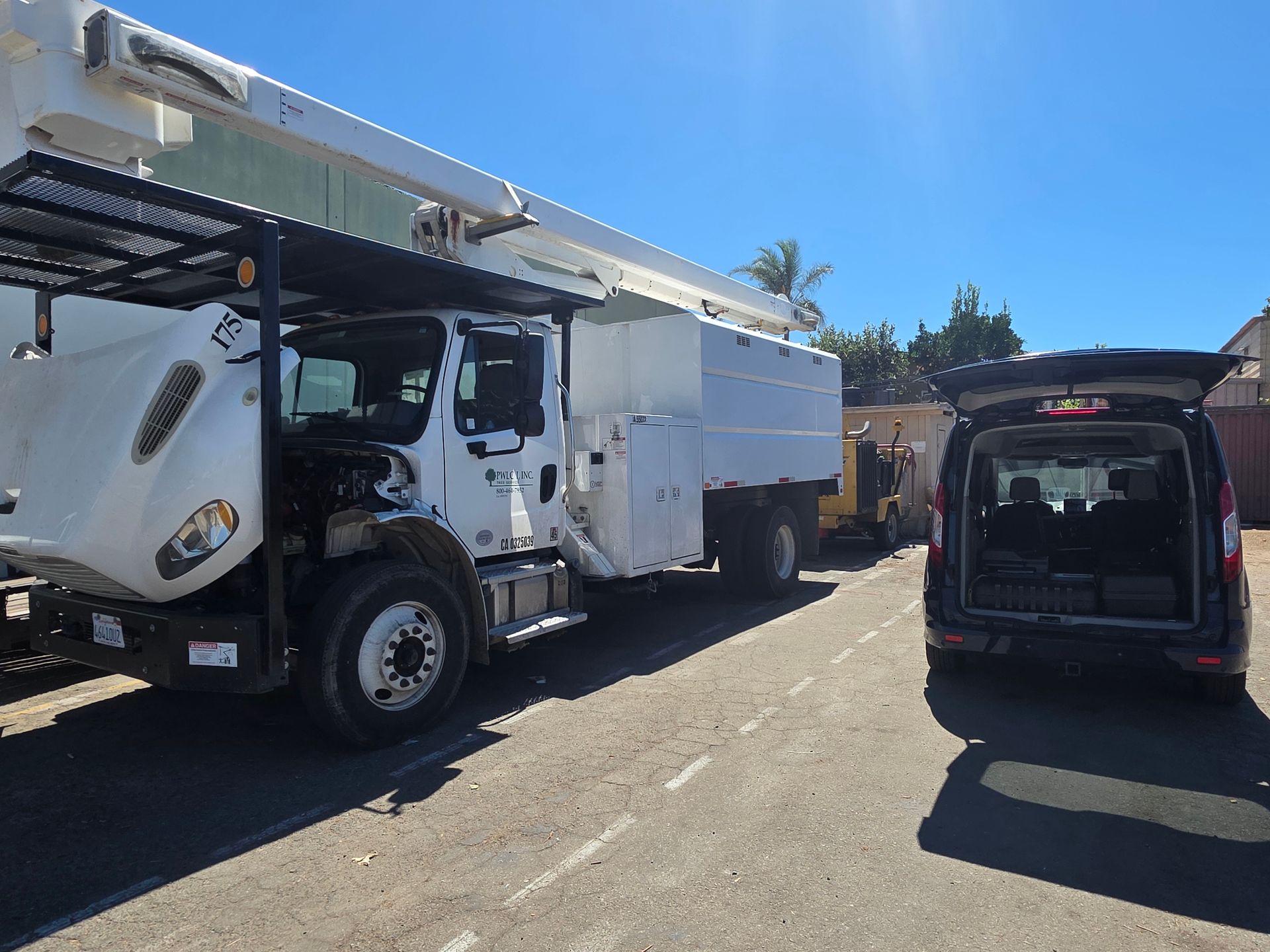 White utility truck and black van parked on a sunny street, with buildings and trees in the background.