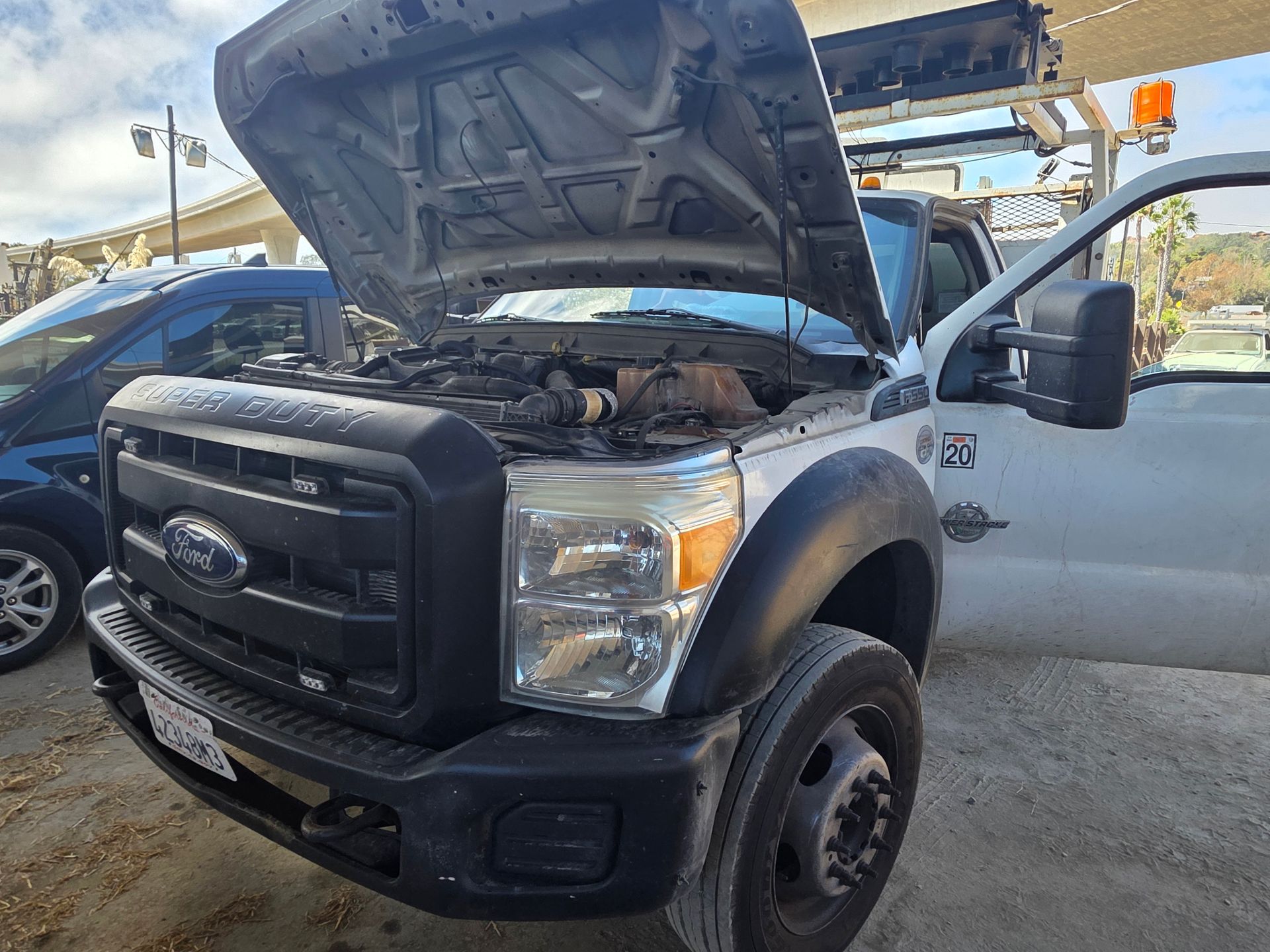 Ford pickup with hood open and driver door open, parked outdoors beside other vehicles
