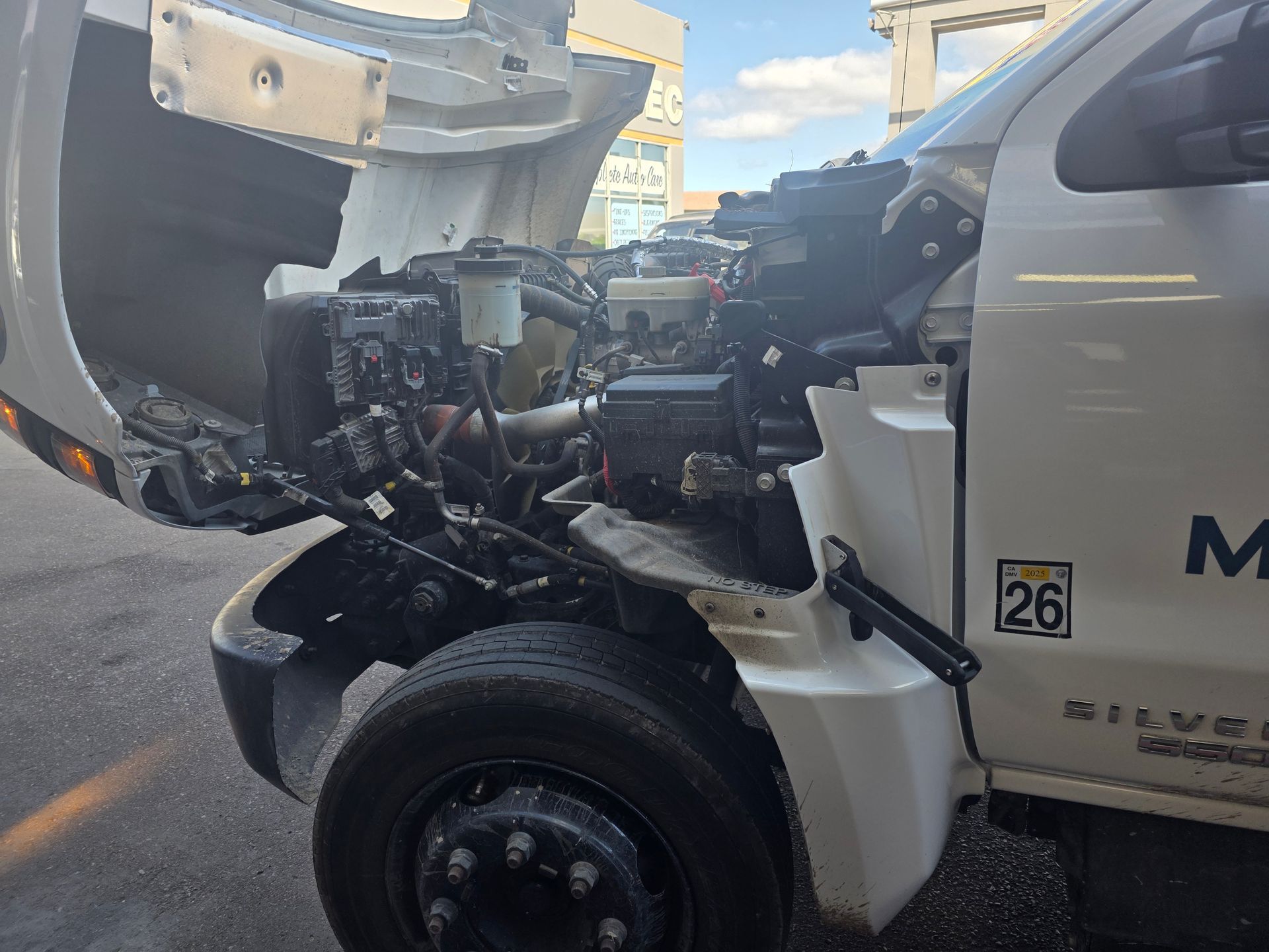 Damaged white tow truck with hood open and front end exposed on a street