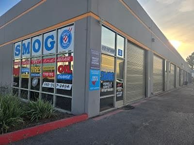 SMOG shop storefront with glass windows, blue signage, and storage unit doors along a sidewalk at sunset