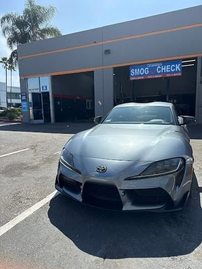 Silver Toyota sports car parked outside a smog check shop in bright daylight.