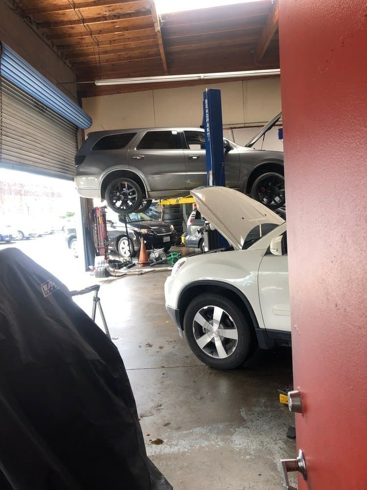 Auto repair garage with a silver SUV lifted on a hoist and a white SUV with its hood open.