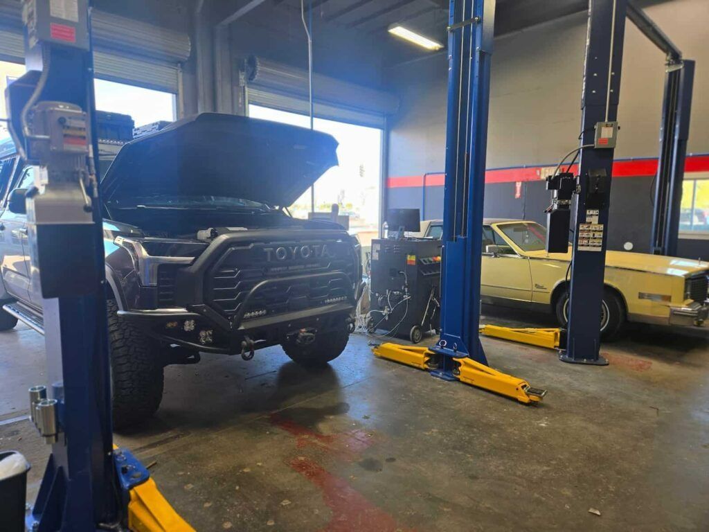 Auto shop with a black truck on a lift and hood open, yellow car in the background.