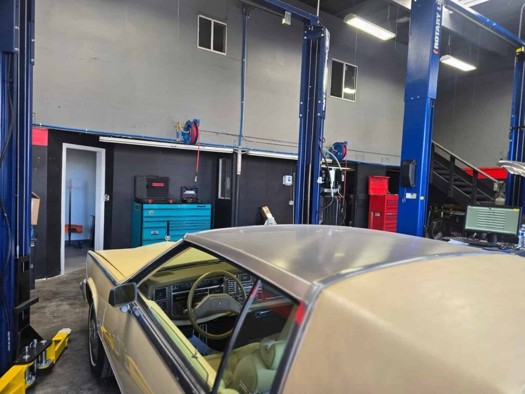Classic car in a garage lift bay with blue hydraulic lifts and shop equipment.