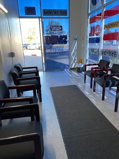 Waiting area with black chairs, a gray carpet, and a glass door with bright daylight outside