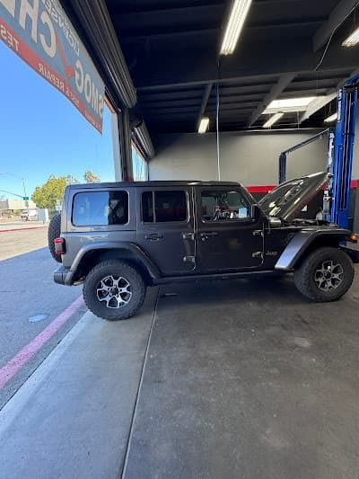 Black Jeep Wrangler parked in a service bay with its hood open.
