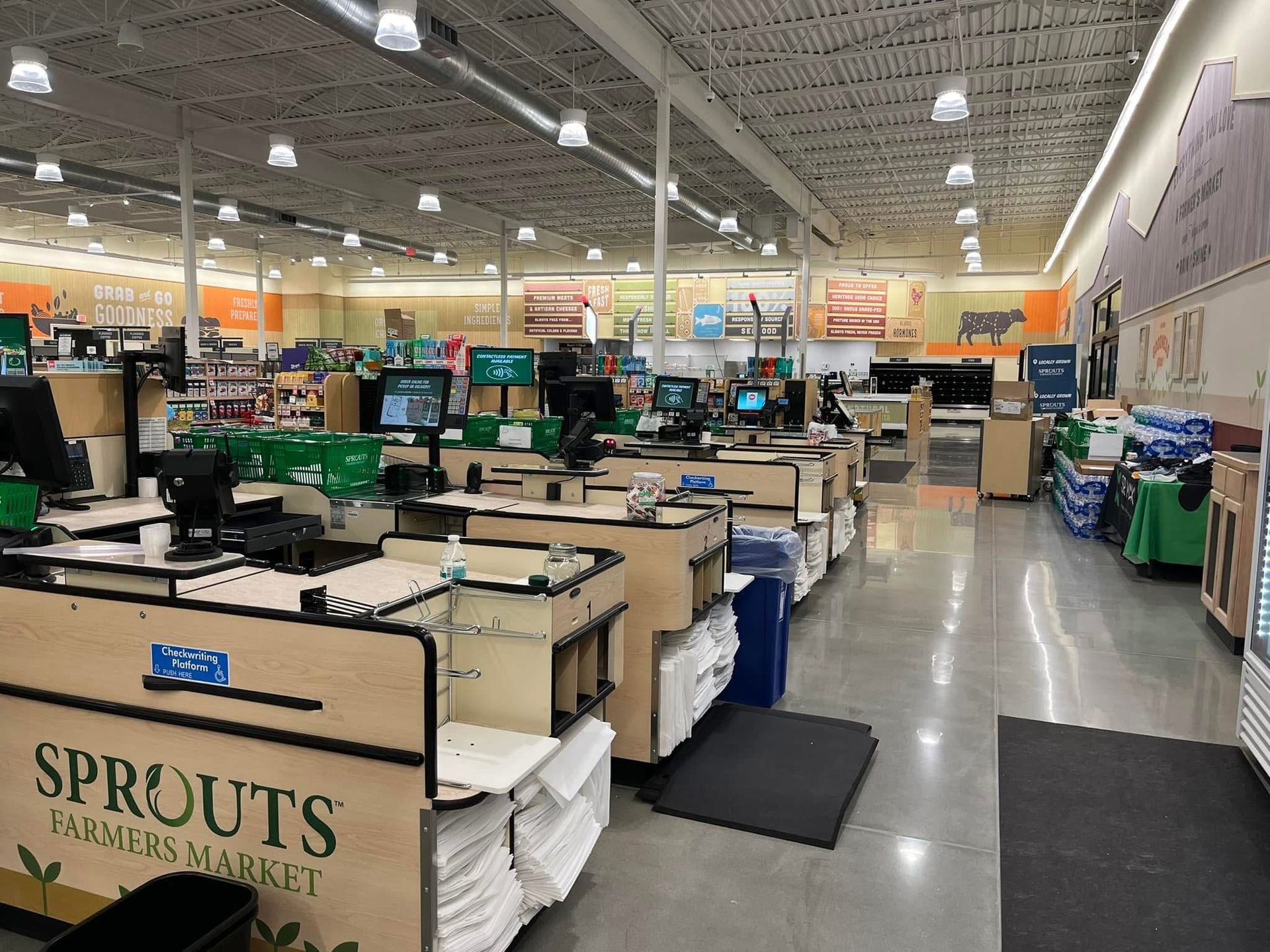 Grocery store checkout area with empty lanes, beige registers, and green bins under bright warehouse lighting