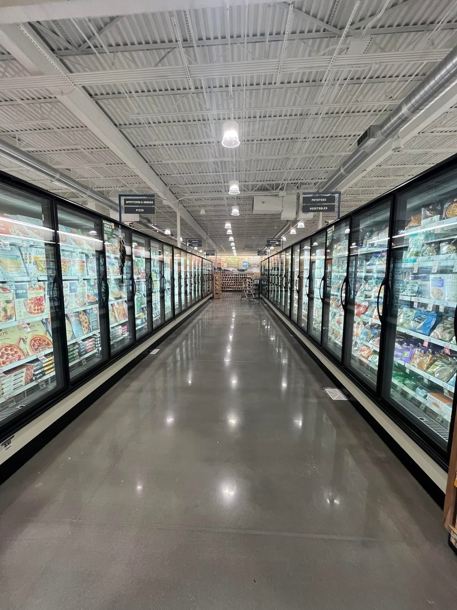 Aisle of a grocery store with glass freezer doors on both sides and polished floor.