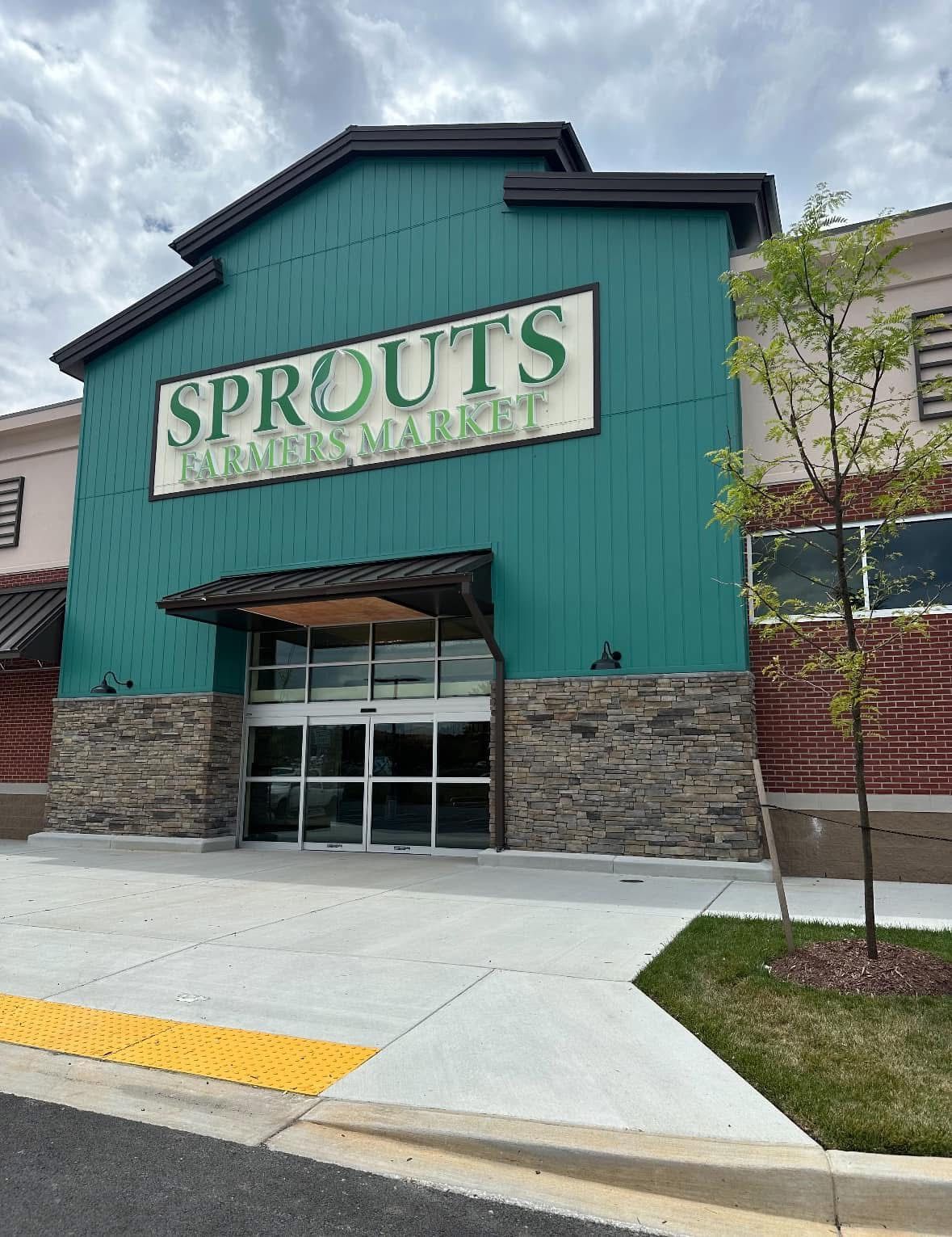 Sprouts grocery store entrance with teal facade, stone accents, and a sidewalk ramp at the front