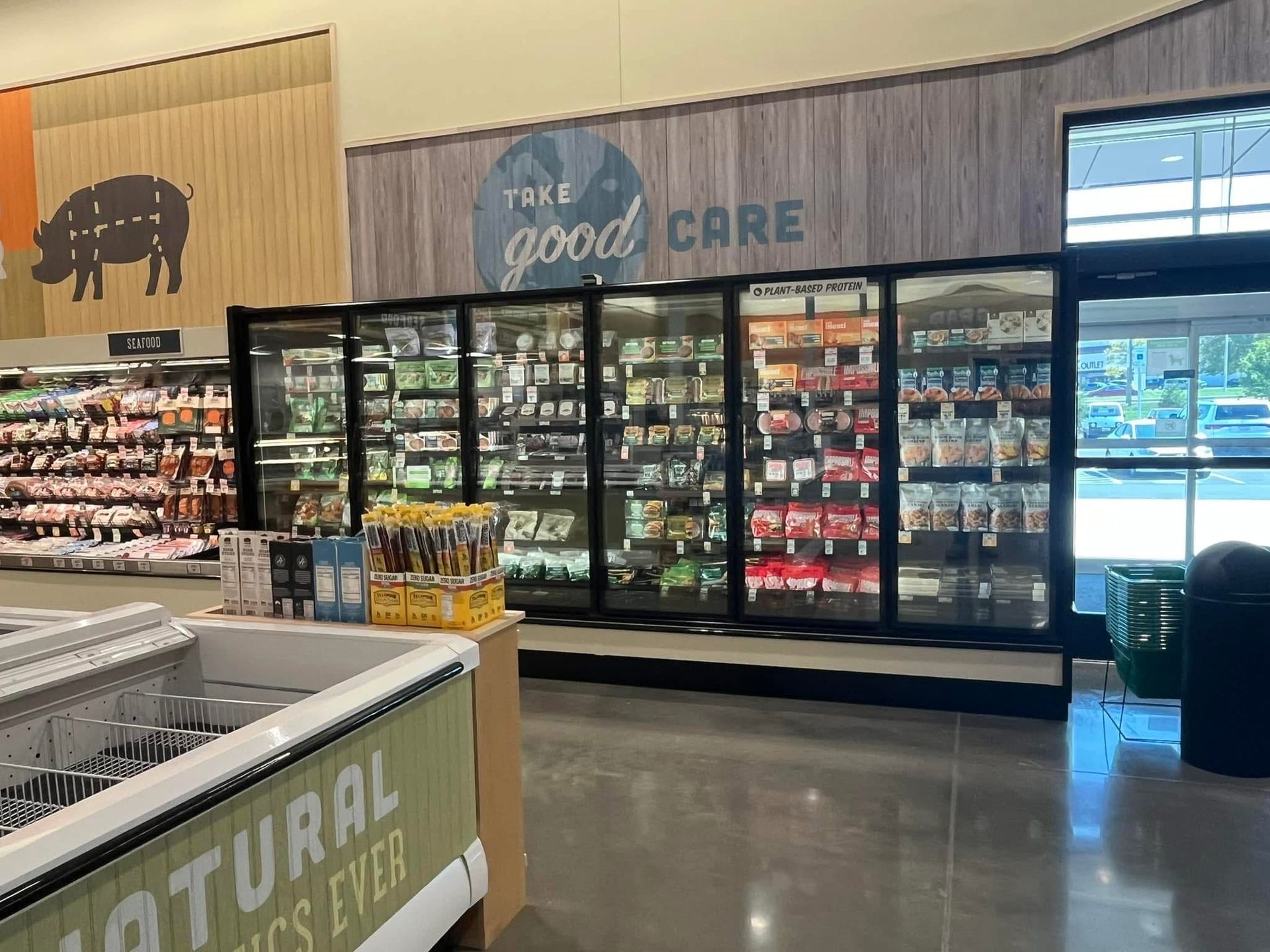 Grocery store aisle with refrigerated pet food cases and a “Take the Good Care” sign