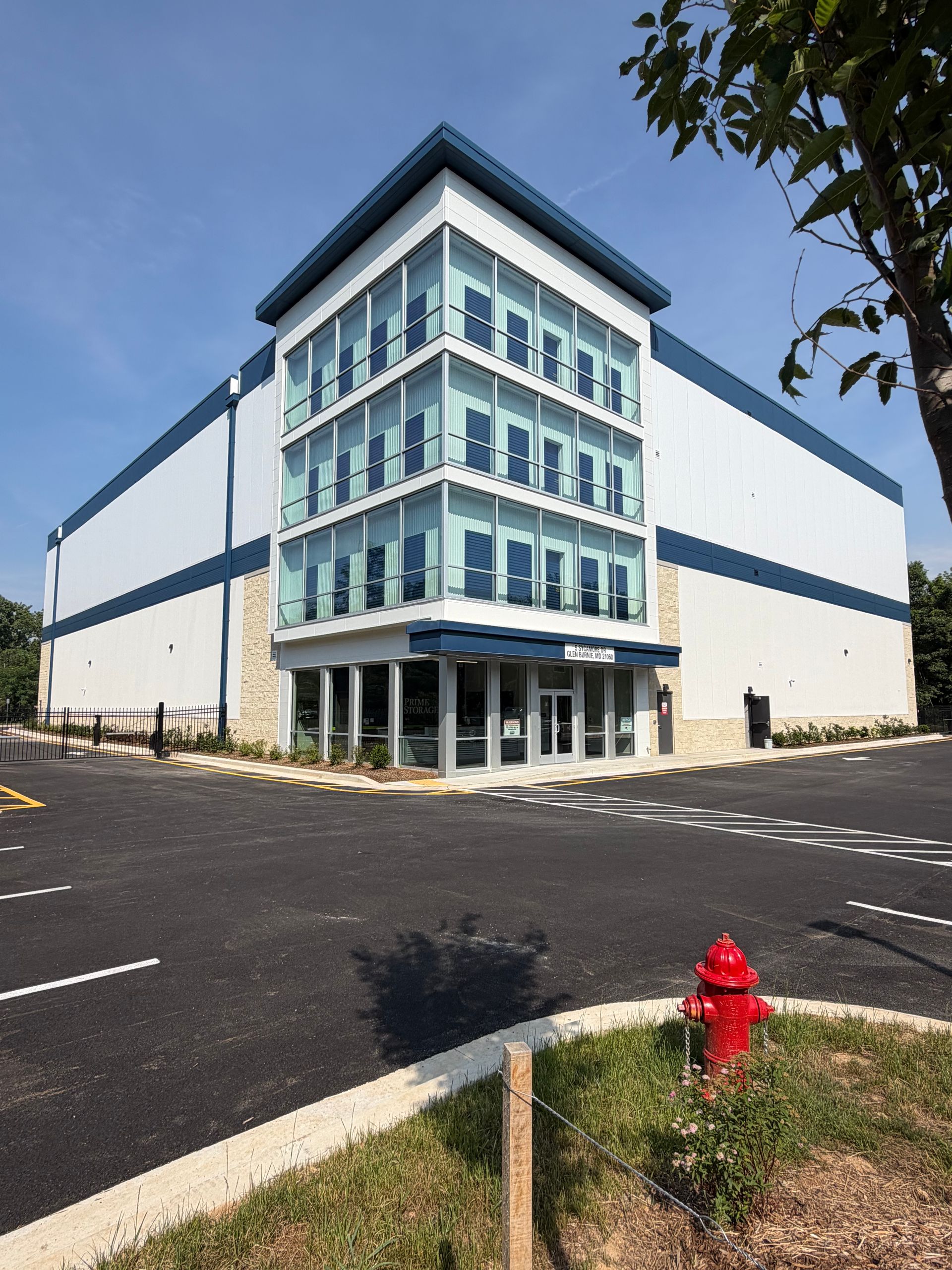 Modern commercial building with blue glass facade, parking lot, and red fire hydrant in front