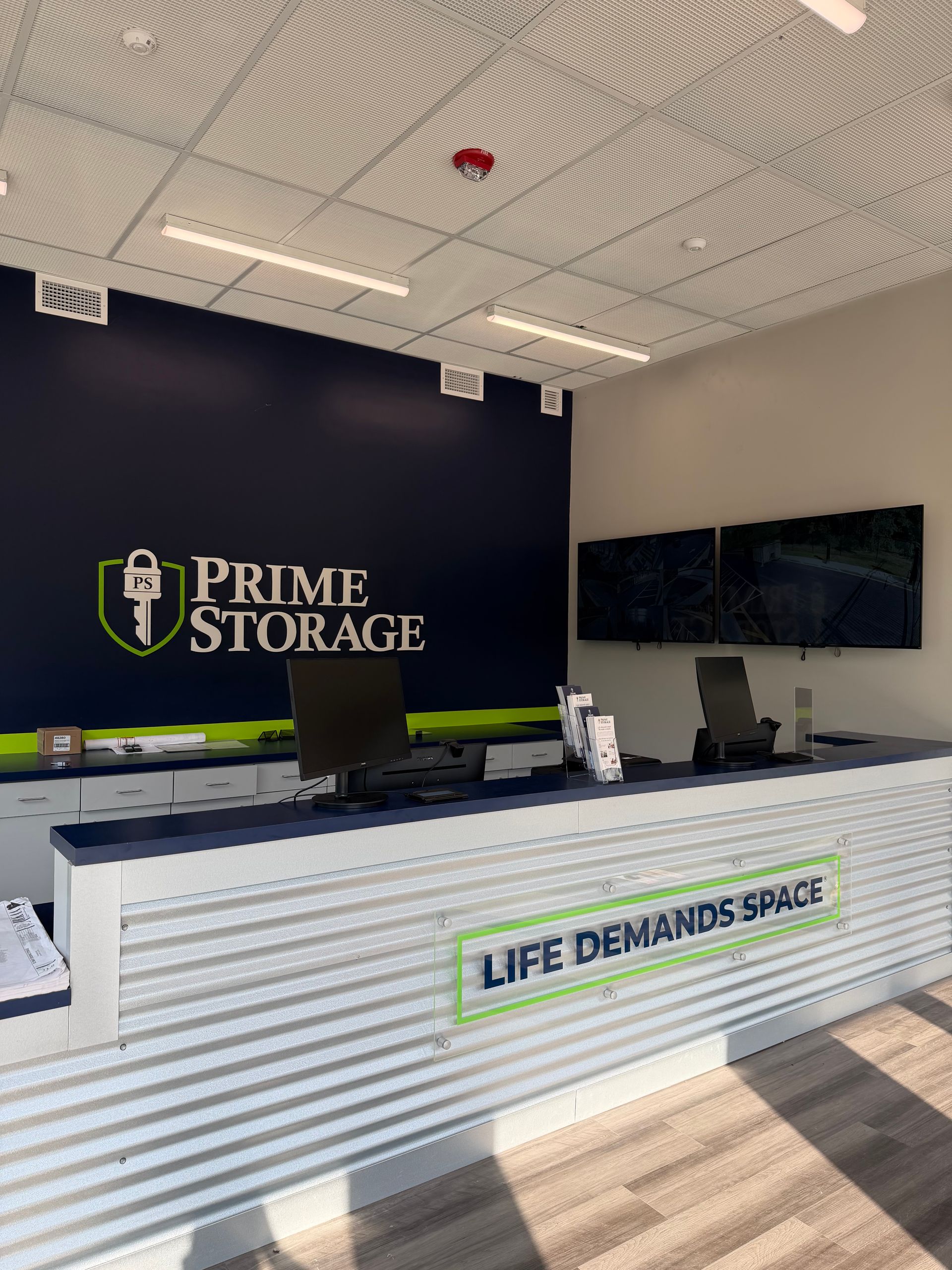 Prime Storage lobby with reception desk, dark accent wall, TV screen, and “Life Demands Space” branding.