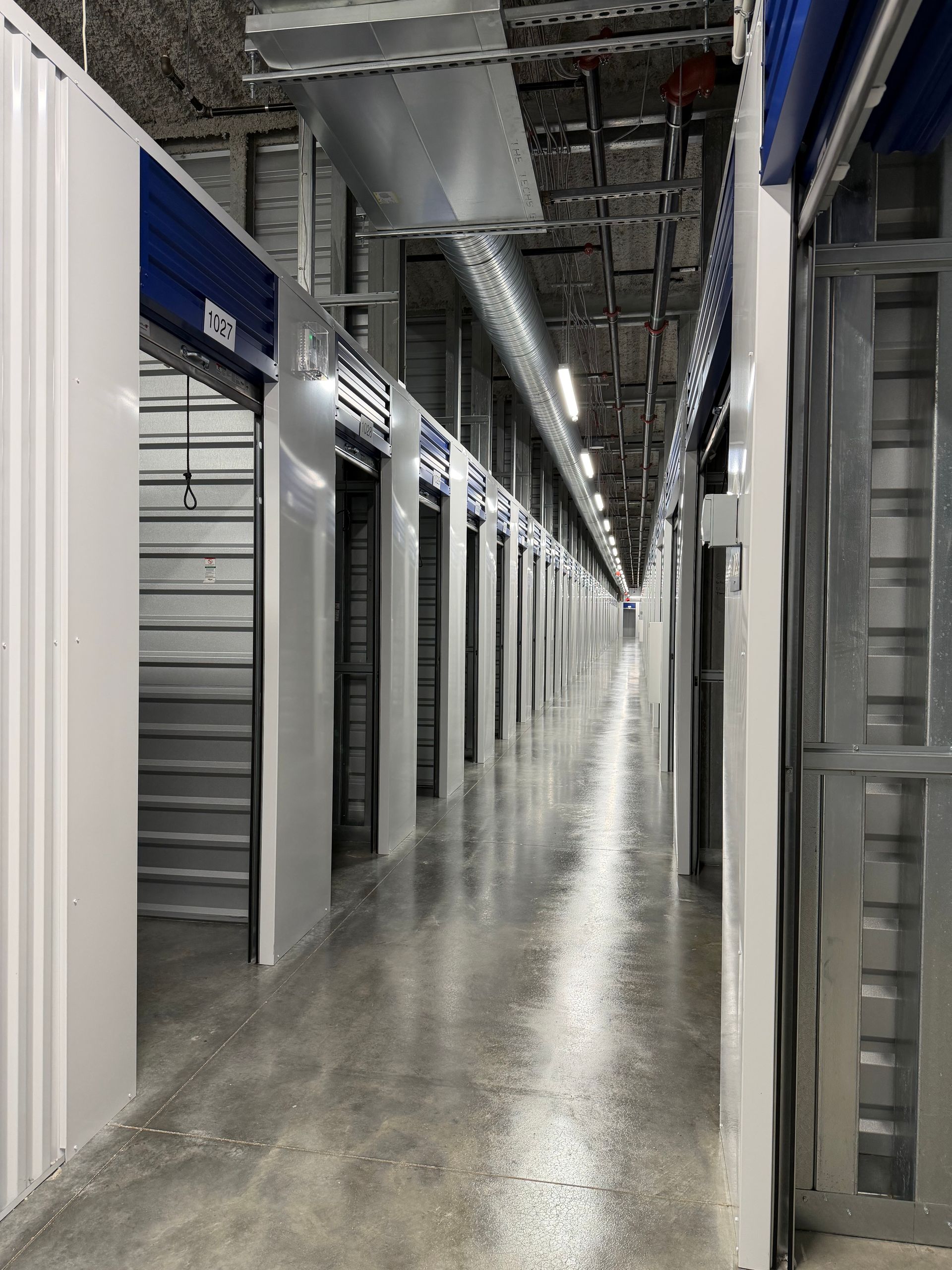 Storage facility corridor with rows of closed metal unit doors and polished concrete floor