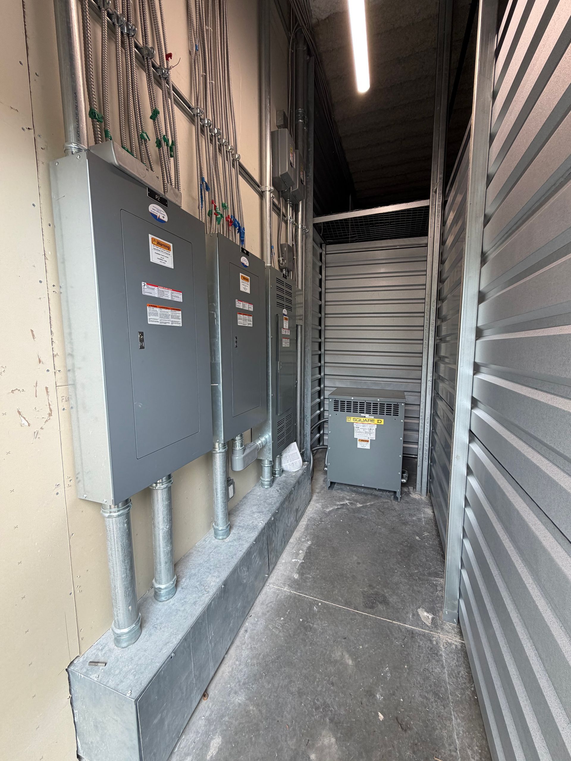 Narrow alley with electrical panels, conduit, and a trash bin under an overhead awning.