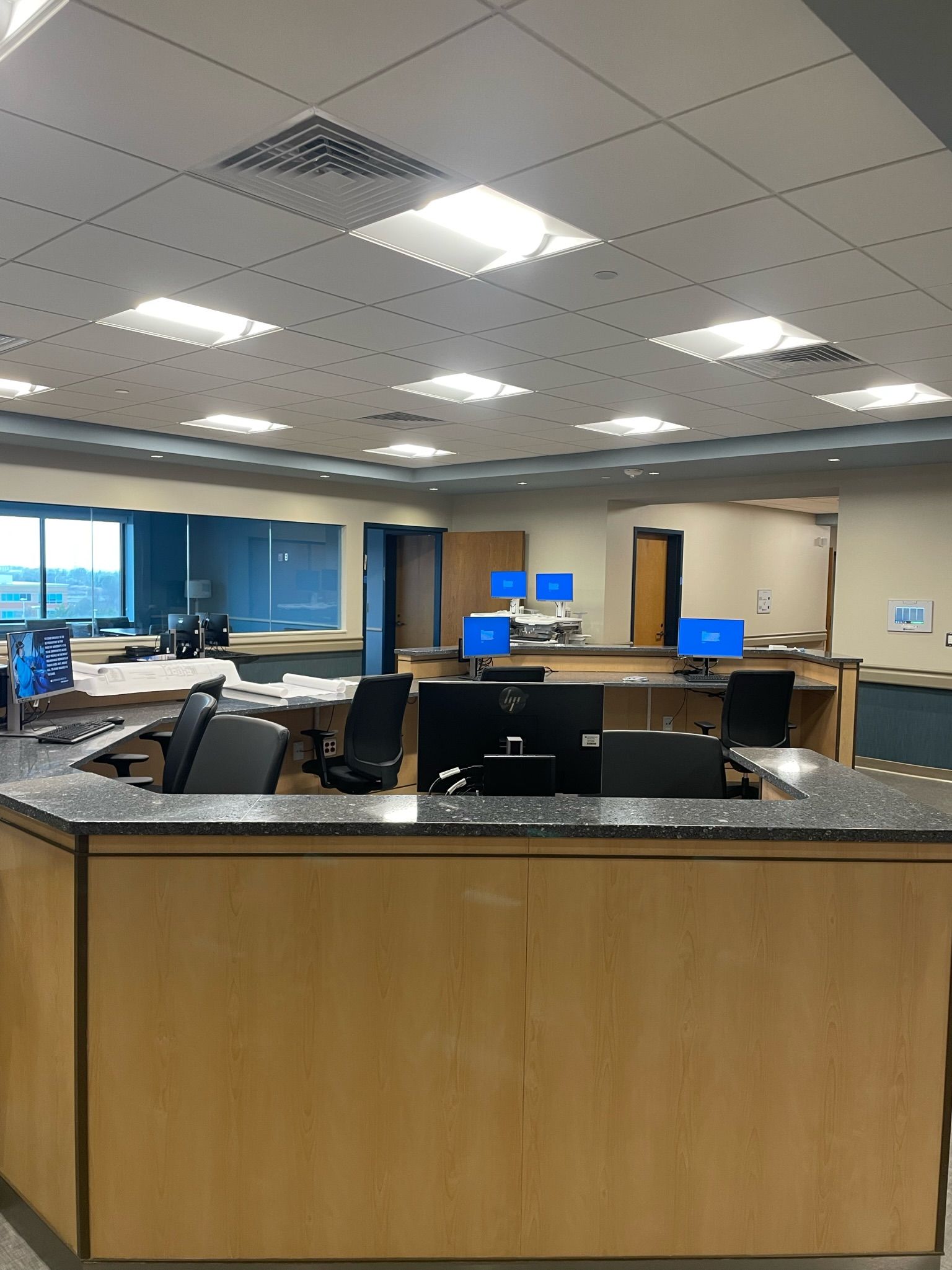 Empty office reception area with desks, blue computer monitors, and overhead fluorescent lights