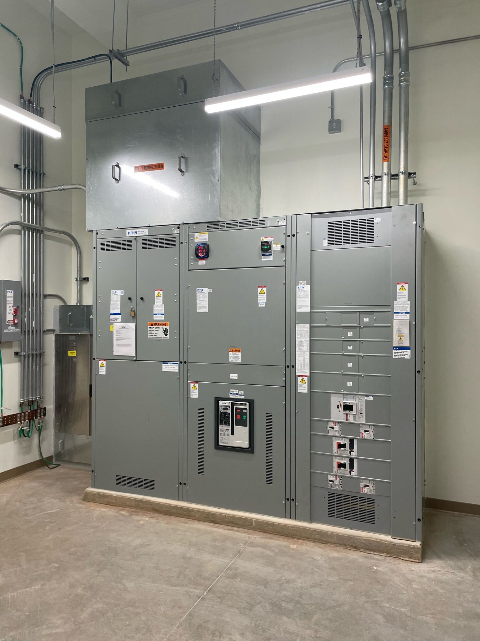 Large gray electrical switchgear cabinets in an industrial utility room with overhead lights.