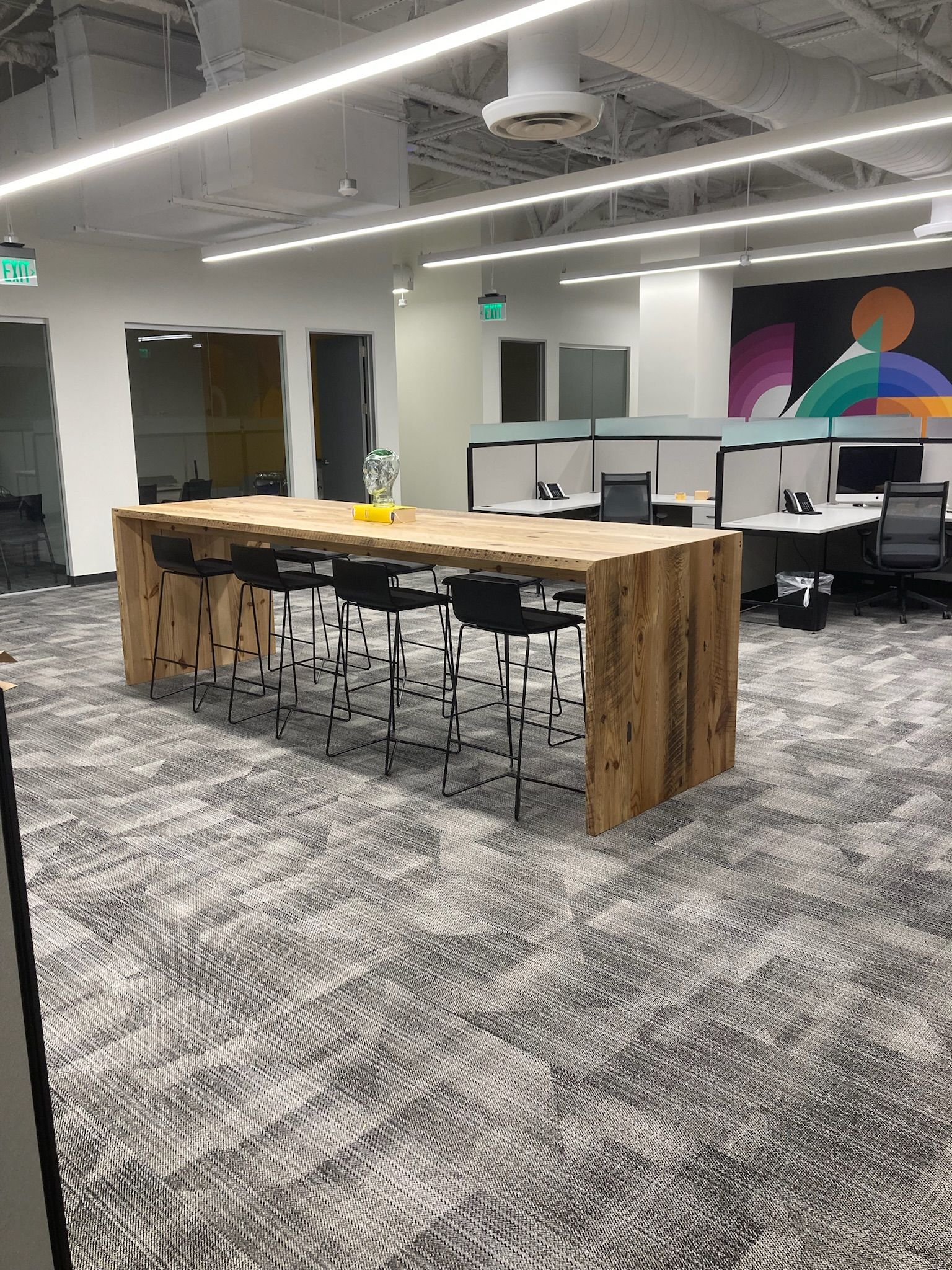 Modern office break area with high table, stools, cubicles, and a colorful wall mural