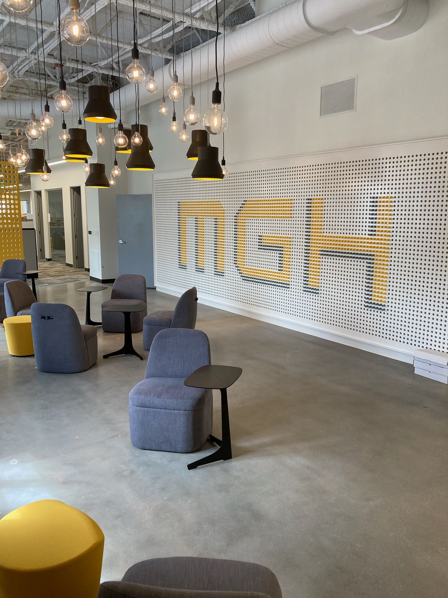 Modern office lounge with hanging lights, gray chairs, and large yellow “MGM” wall lettering
