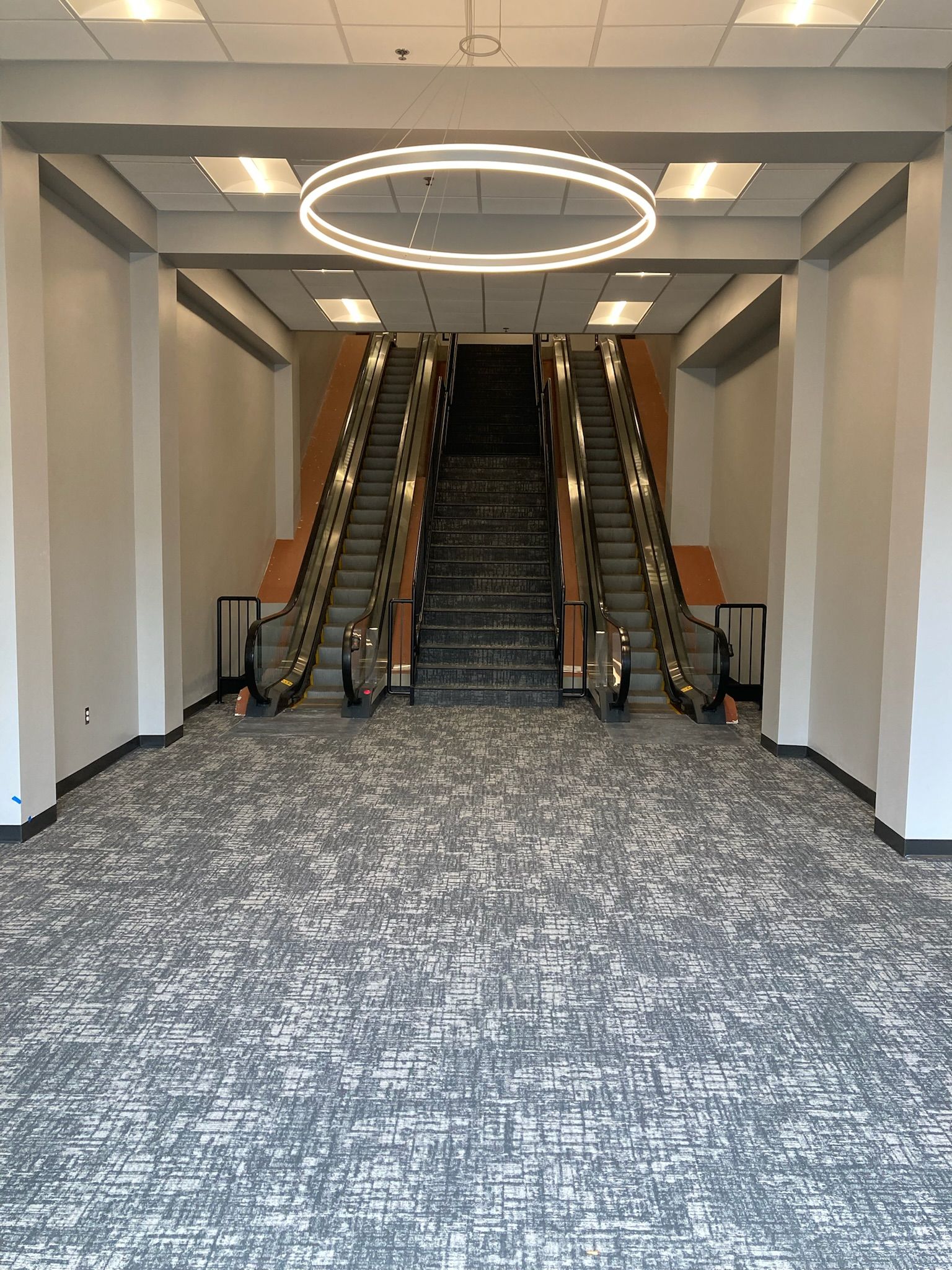 Empty lobby with twin escalators, a central staircase, and a large circular ceiling light