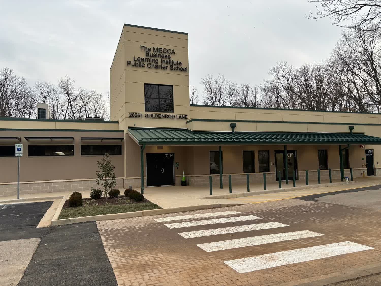 School entrance with beige facade, green awning, and crosswalk in front
