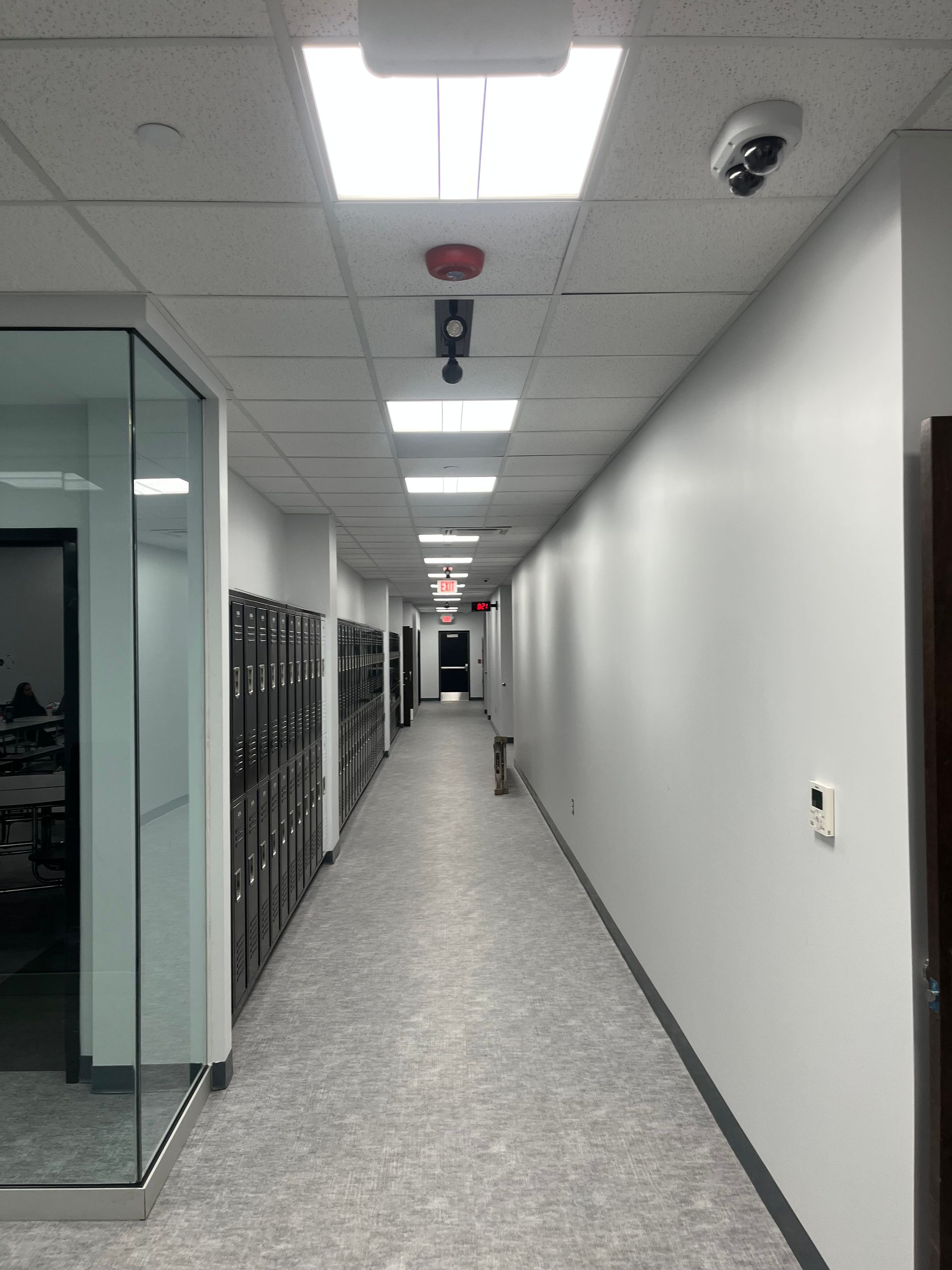 Long office hallway with glass-walled rooms, ceiling lights, and storage cabinets along one side