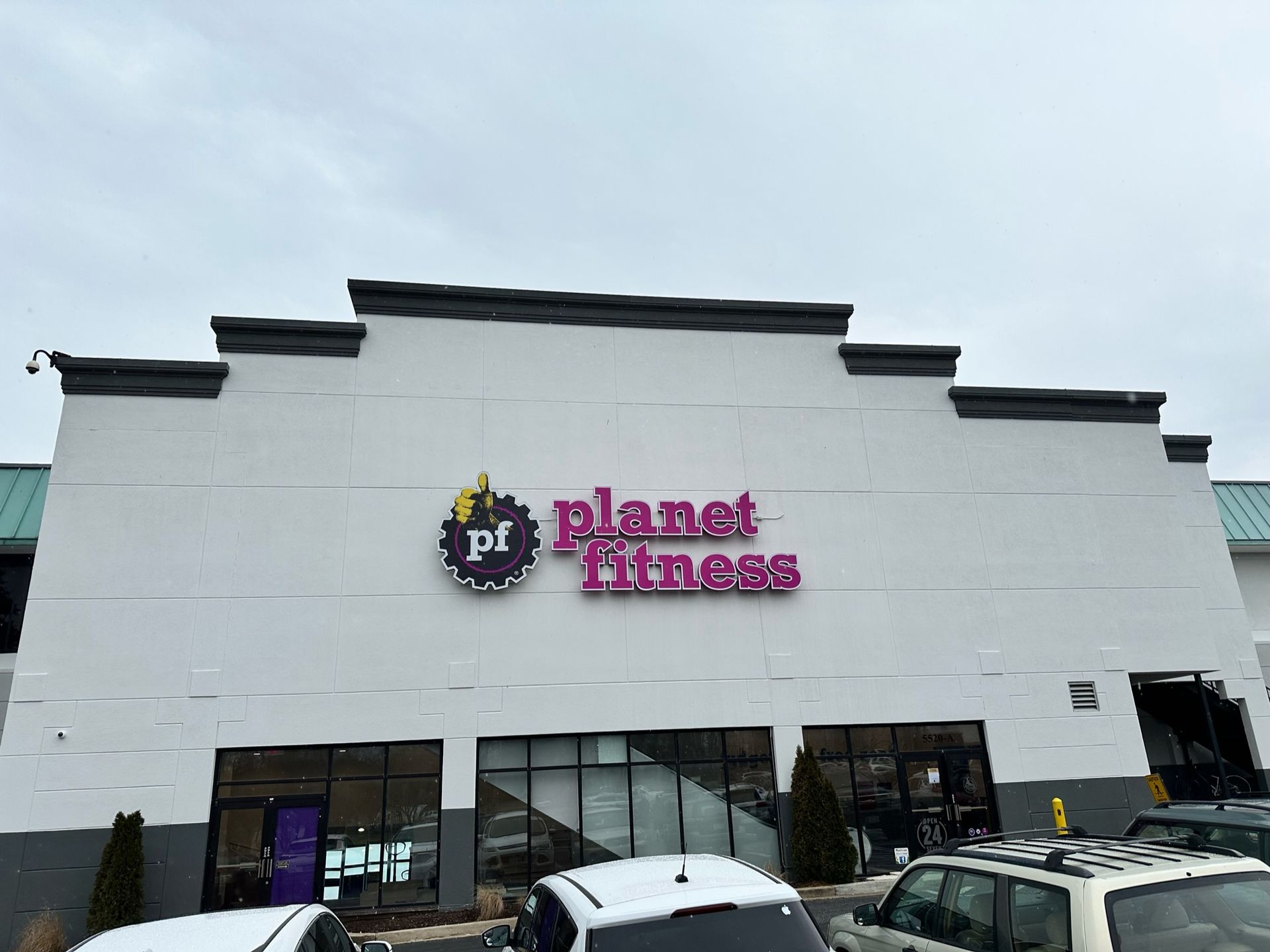 Planet Fitness storefront with white facade and purple logo above parked cars