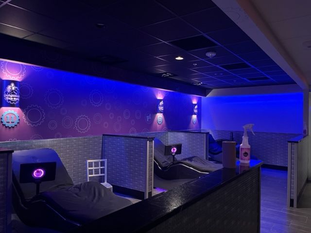 Dimly lit blue lounge with pod-style reclining chairs and partitions under a dark ceiling