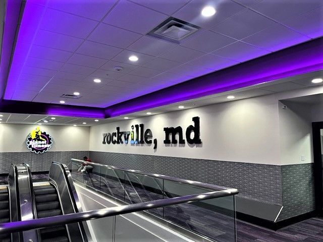 Modern airport concourse with escalators, purple ceiling lights, and 