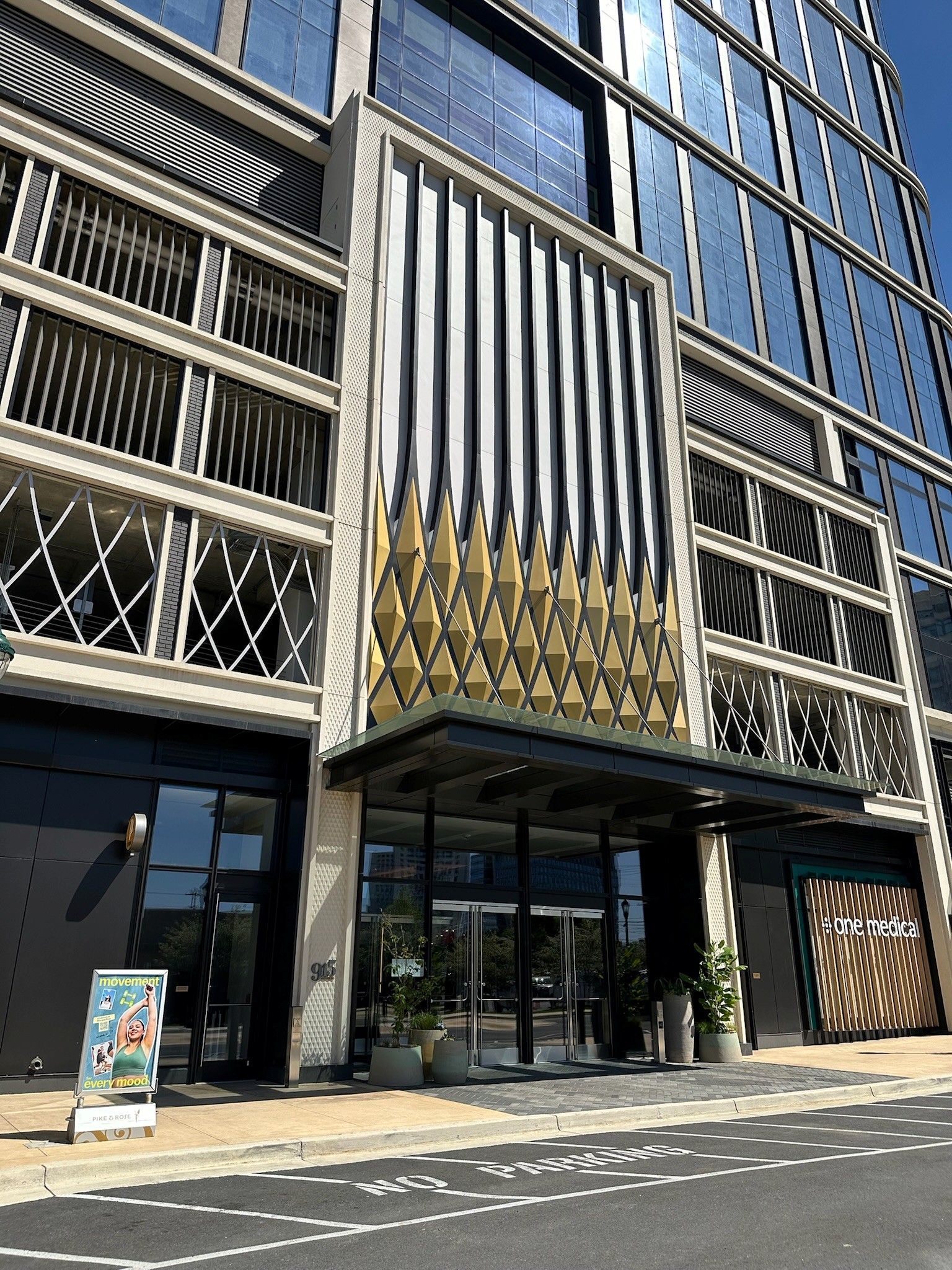 Modern glass office building entrance with gold vertical accents and sidewalk out front