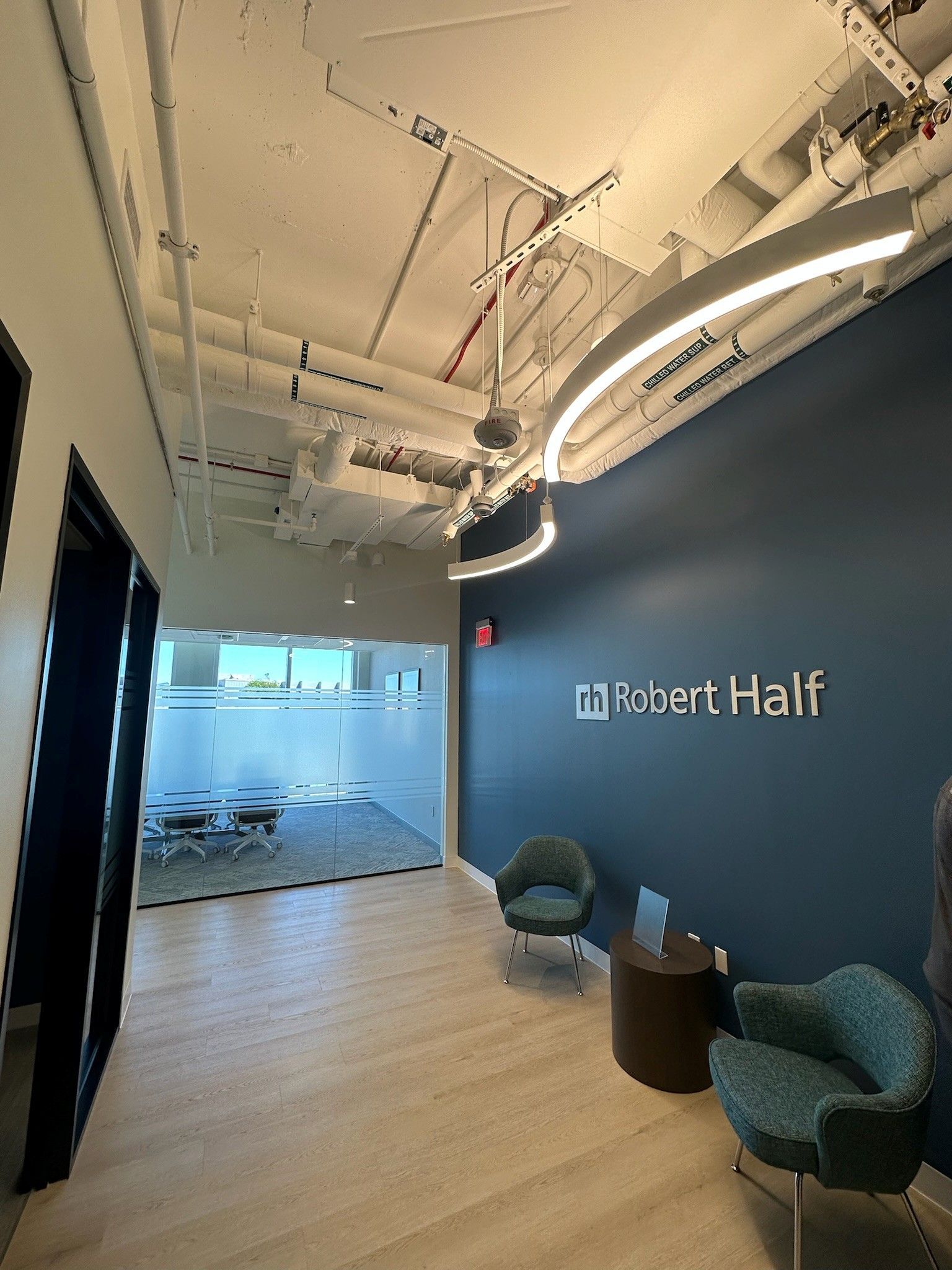 Modern office lounge with blue walls, chairs, glass meeting room, and Robert Half sign