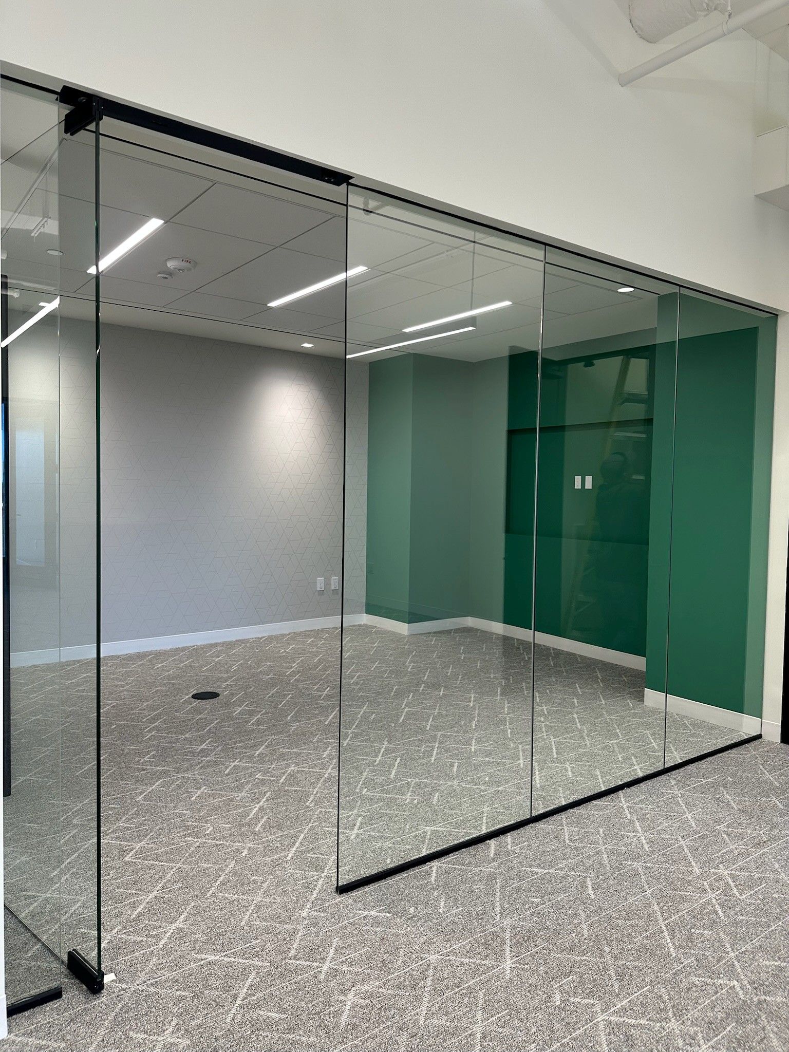 Empty modern office with glass partition walls and green-tinted doors on a gray carpeted floor