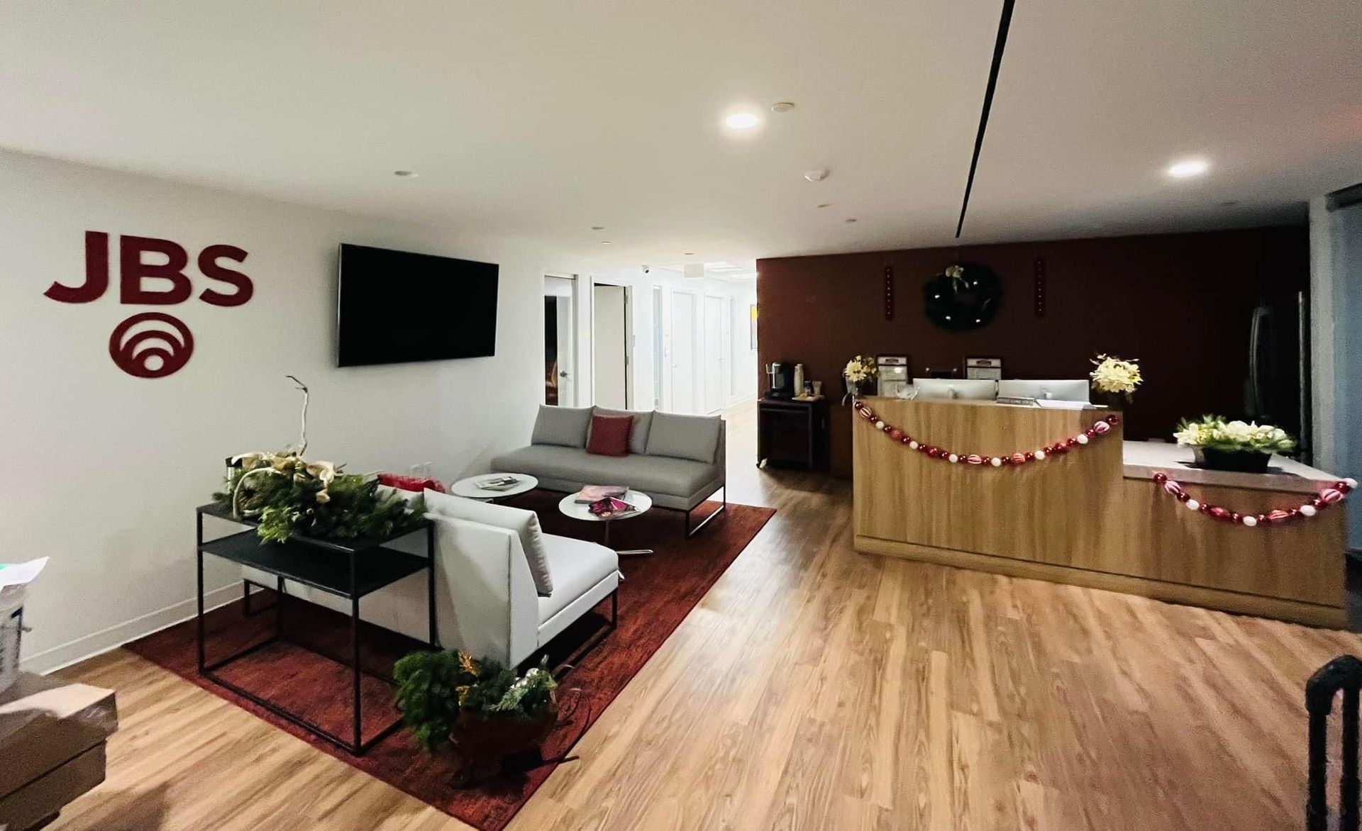 a living room with a couch, table, television and JBS logo on the wall