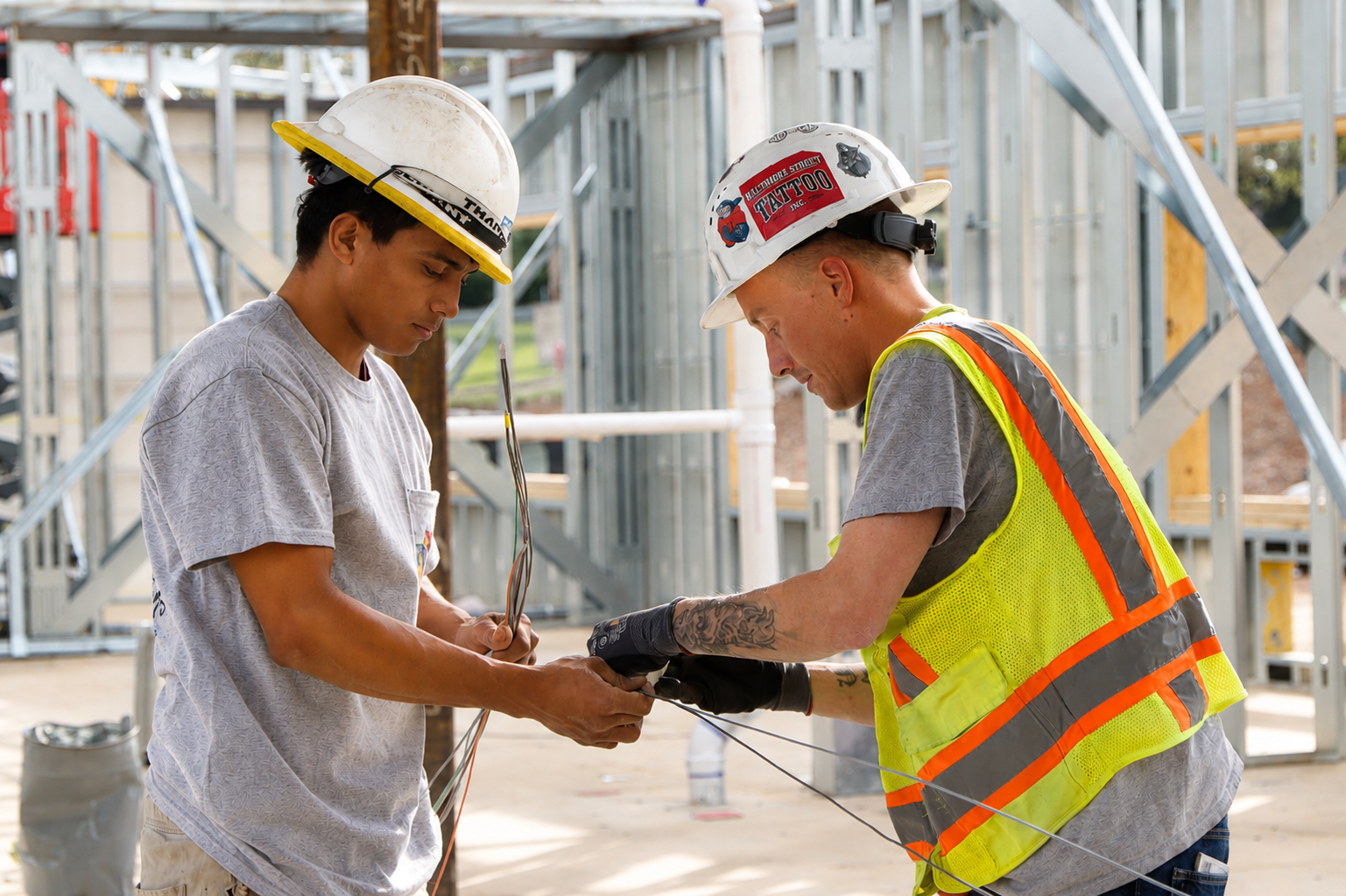 Two construction workers in hard hats adjusting a tool at a building site