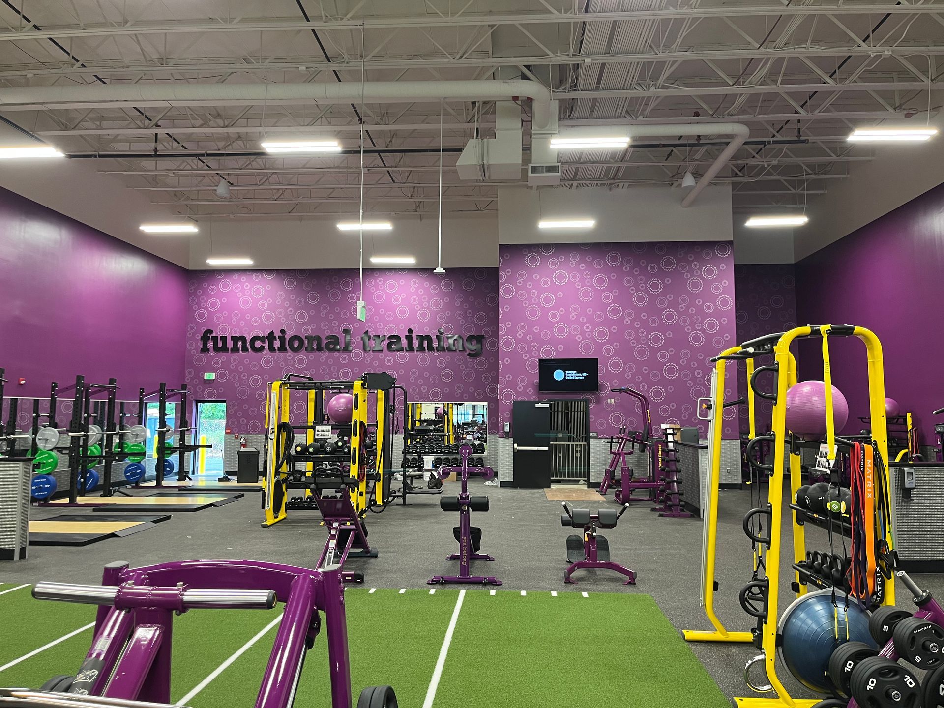 Purple gym interior with weight machines, benches, and turf flooring under bright overhead lights