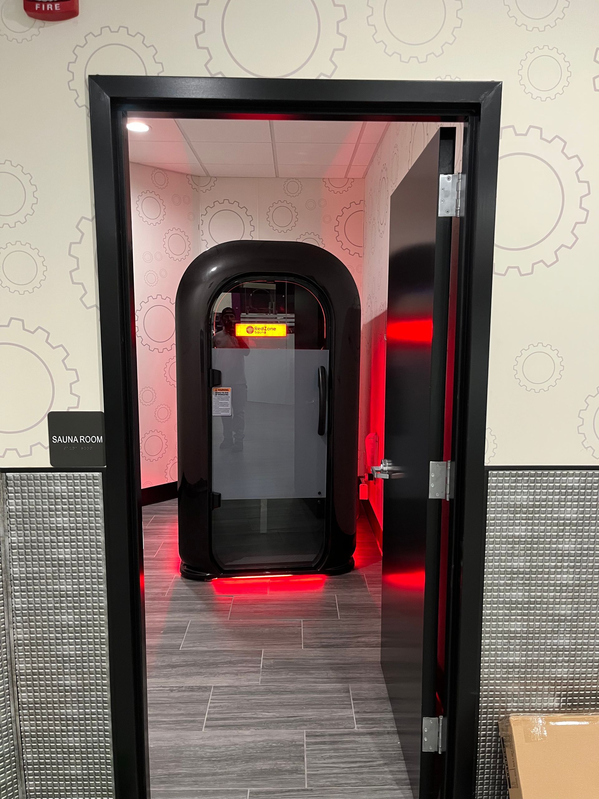 Black doorway opening to a dim room with a red-lit arcade cabinet and patterned wallpaper.