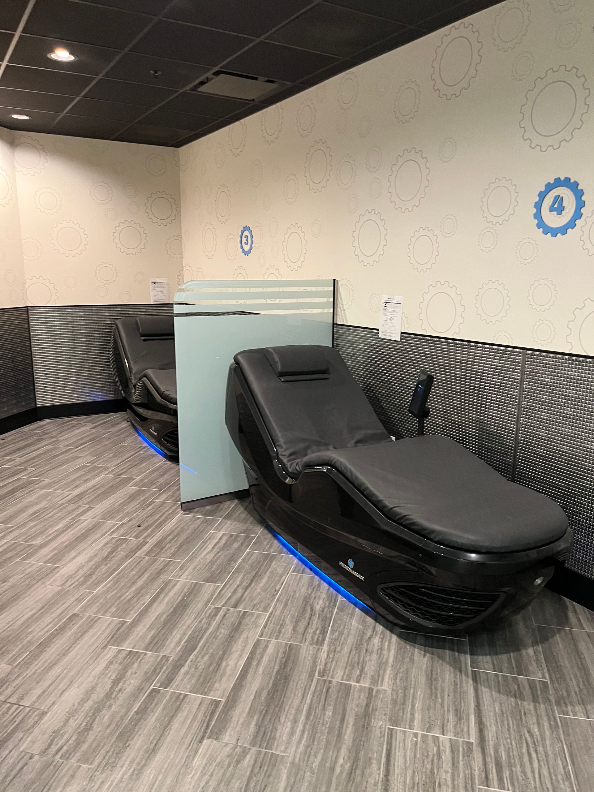 Massage table in a dim room with gray walls, wood floor, and blue accent lighting.