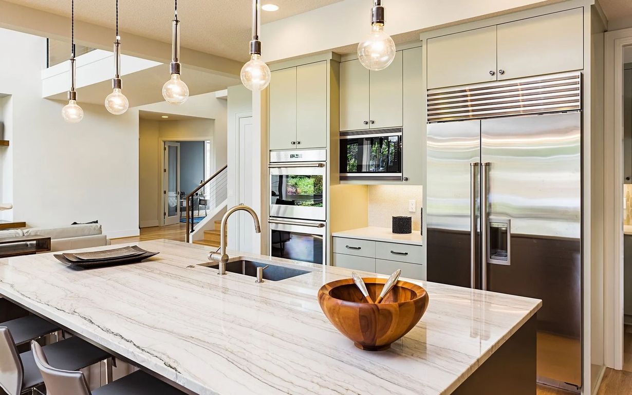 Modern kitchen with large island, light cabinets, stainless steel appliances, and pendant lights.
