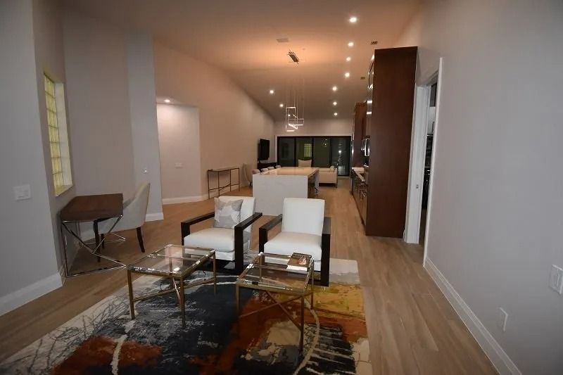 Modern living room with chairs, rug, and kitchen in the background.