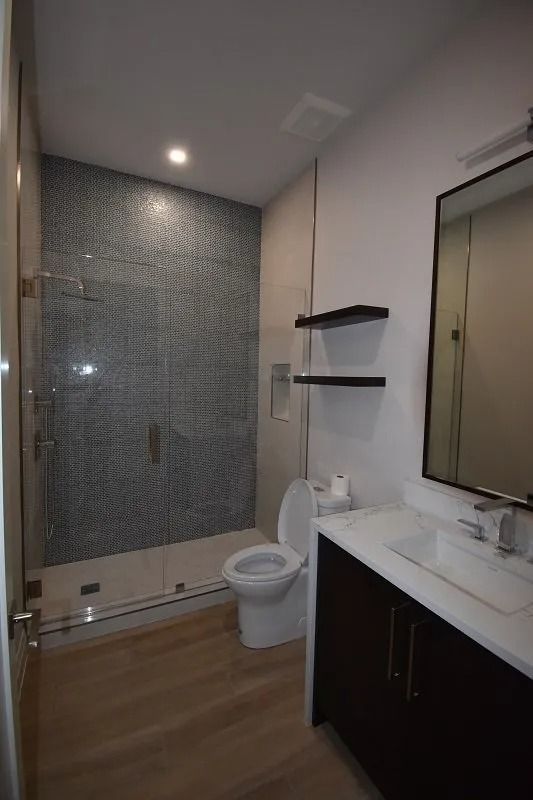 Modern bathroom with blue mosaic shower wall, toilet, vanity, and floating shelves.