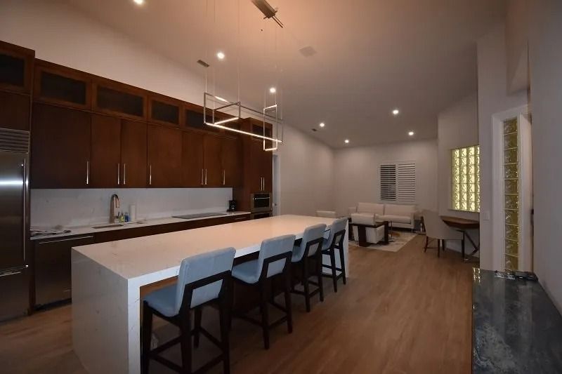 Modern kitchen with large island, dark wood cabinets, and seating; living area in the background.
