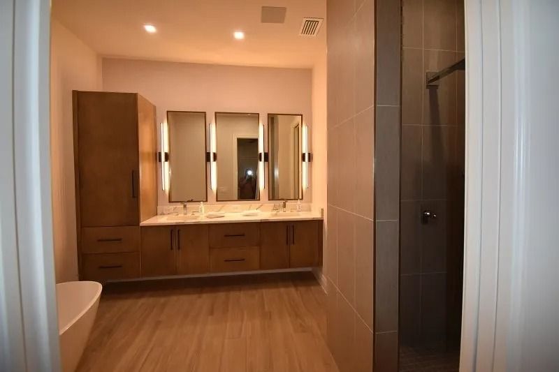 Bathroom with double vanity, tall cabinet, and shower. Light wood cabinets, beige tile, neutral colors.