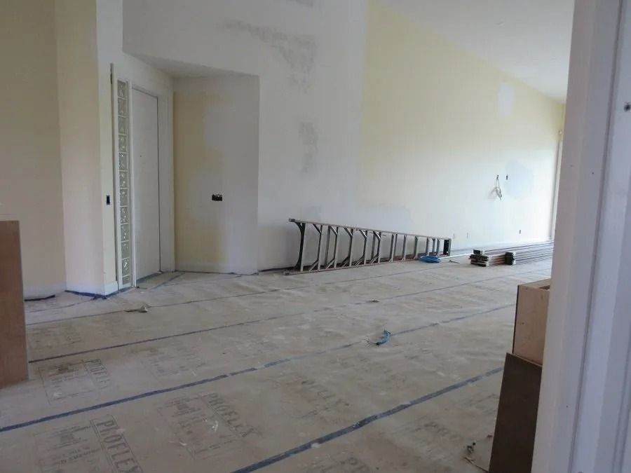 Room under construction: light-colored walls, exposed floorboards, a ladder, and a partially open door.