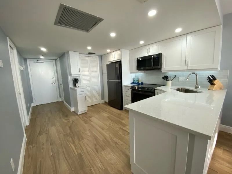 White kitchen with light wood floors, white cabinets, black appliances, and a white countertop.