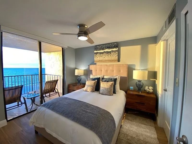Bedroom with bed, balcony overlooking the ocean, ceiling fan, and artwork.